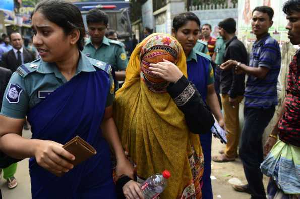 Bangladeshi security personnel escort Nritto Shahadat, the wife of cricketer Shahadat Hossain, towards a court appearance after her arrest in Dhaka.