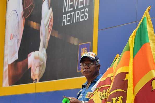 A Sri Lankan vendor with national flags while he stands beside a banner featuring an image of Mahela Jayawardene.